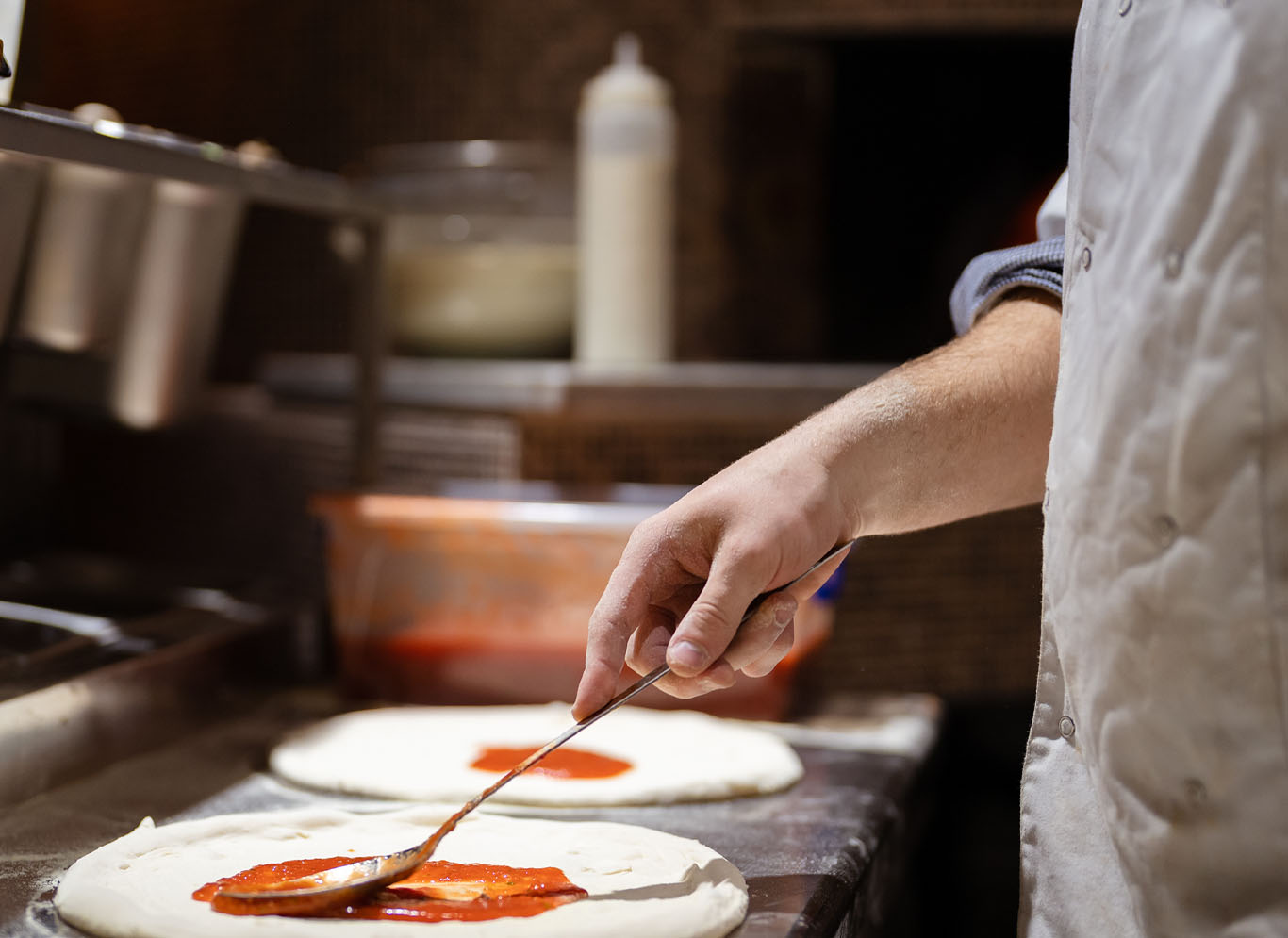 chef placing sauce on pizza